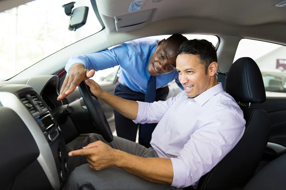 Car salesman showing new car interior to customer sitting