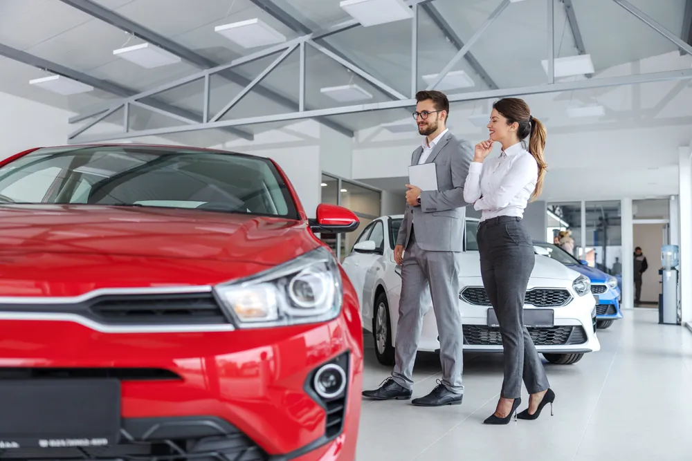 Male car sales rep and female customer looking at red car