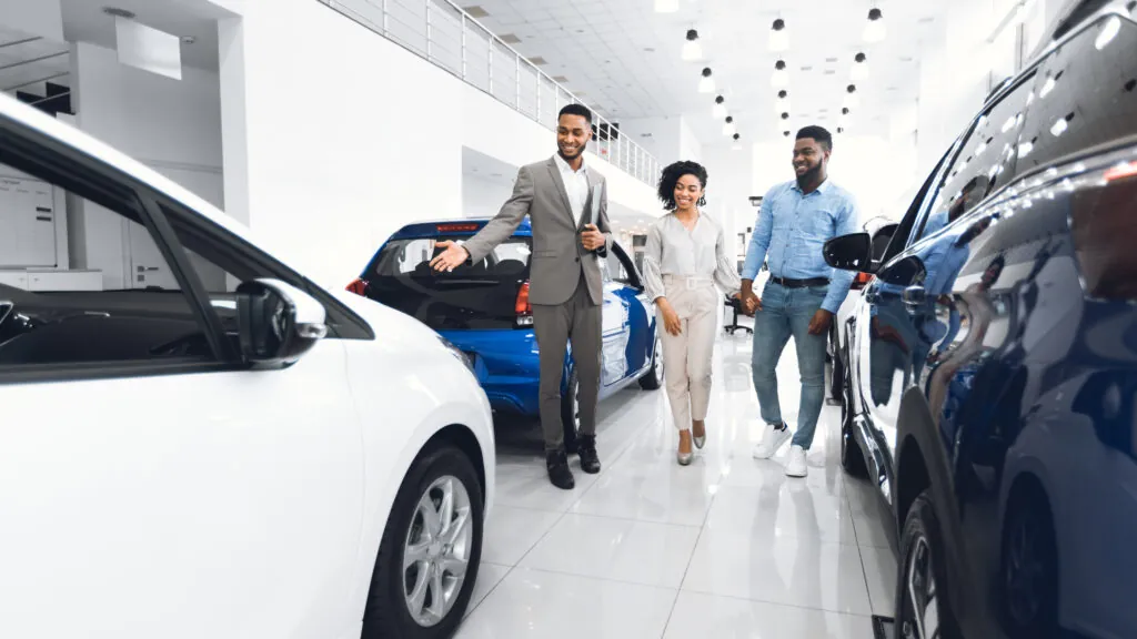 Salesperson in an auto showroom, selling a vehicle to two customers