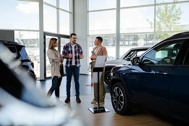 man and woman shopping in a car dealership talking to a female salesperson